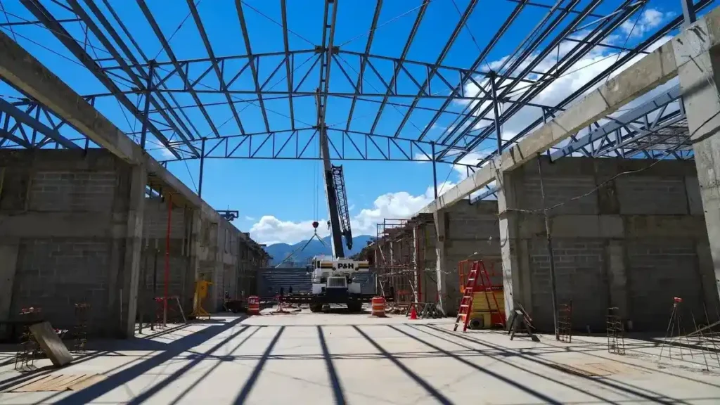 Estructura interna de acero y concreto durante las obras de la megacárcel CACCO, destacando el uso de maquinaria pesada y techado de alta resistencia.