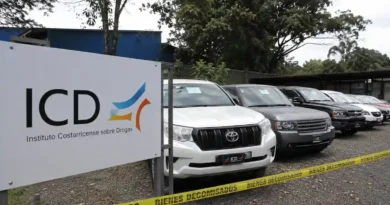 Rótulo del Instituto Costarricense sobre Drogas junto a una fila de automóviles de lujo custodiados por una cinta amarilla de vehículos decomisados al narcotráfico.